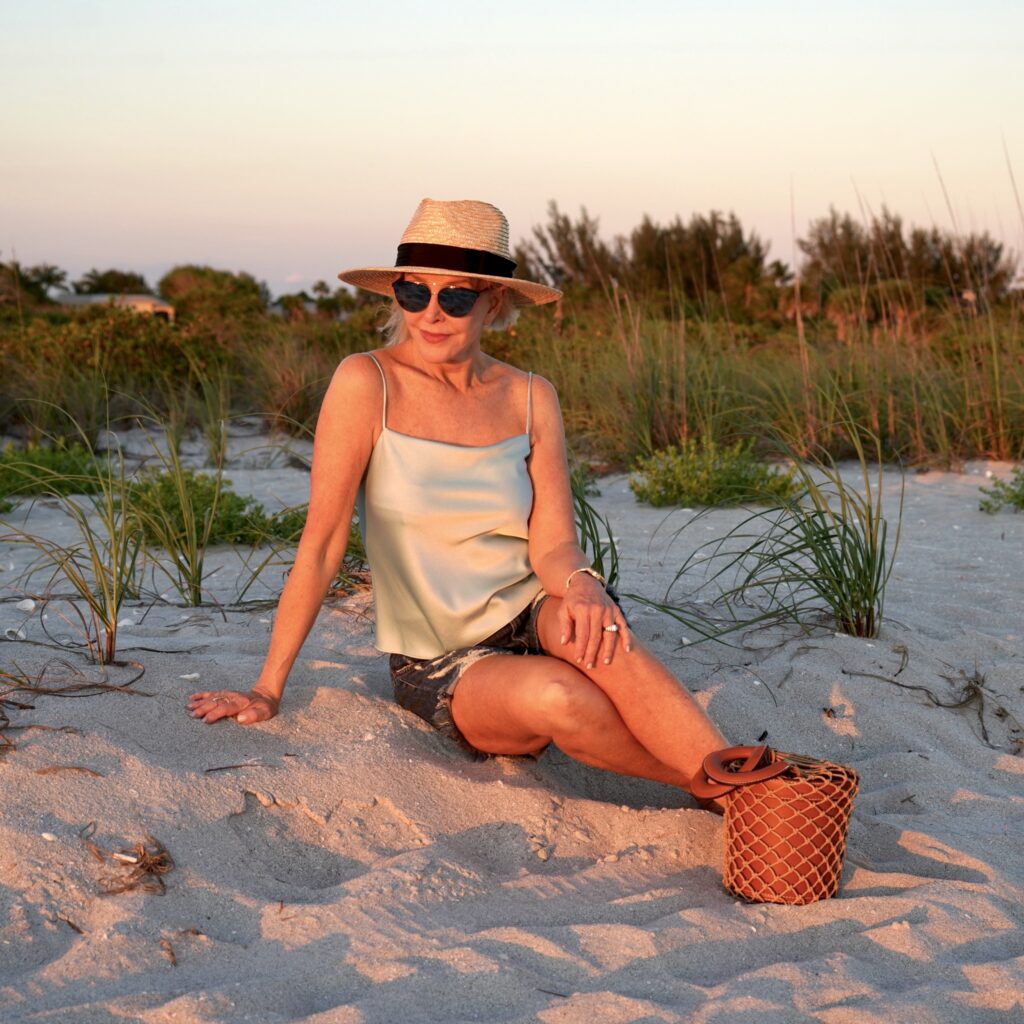 Sheree Frede of the SheShe Show Sitting on the beach wearing a Panama Hat