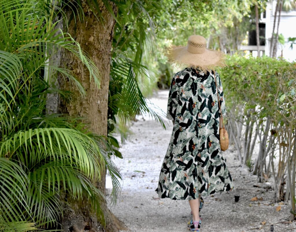 Sheree Frede of tSheree Frede of the SheShe Show walking on the beach weraring a long white dress and straw hat