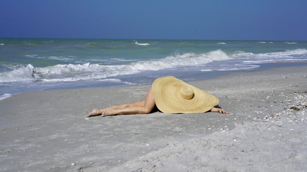 Sheree Frede of tSheree Frede of the SheShe Show laying down on the beach under a very large straw hat