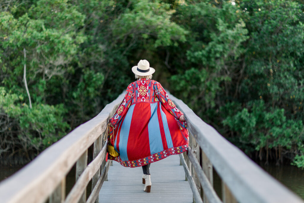 Sheree Frede of the SheShe Show walking on footbridge wearing a long duster and Panama Hat