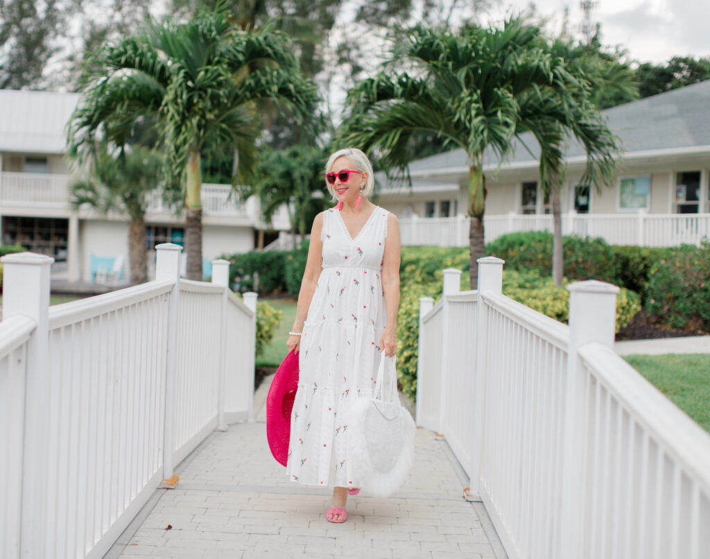 Sheree Frede of the SheShe Show walking on white bridge wearing a white maxi dress and hot pink hat