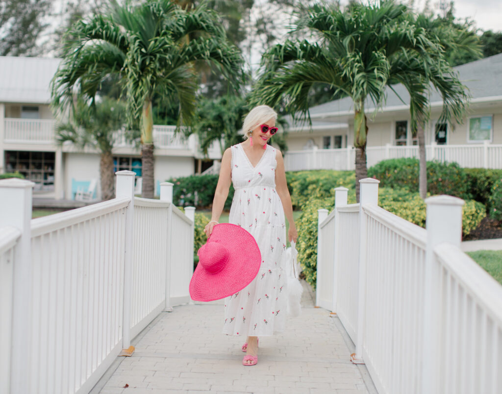 Sheree Frede of the SheShe Show walking on white bridge wearing a white maxi dress and hot pink hat