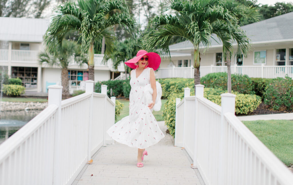 Sheree Frede of the SheShe Show walking on white bridge wearing a white maxi dress and hot pink hat