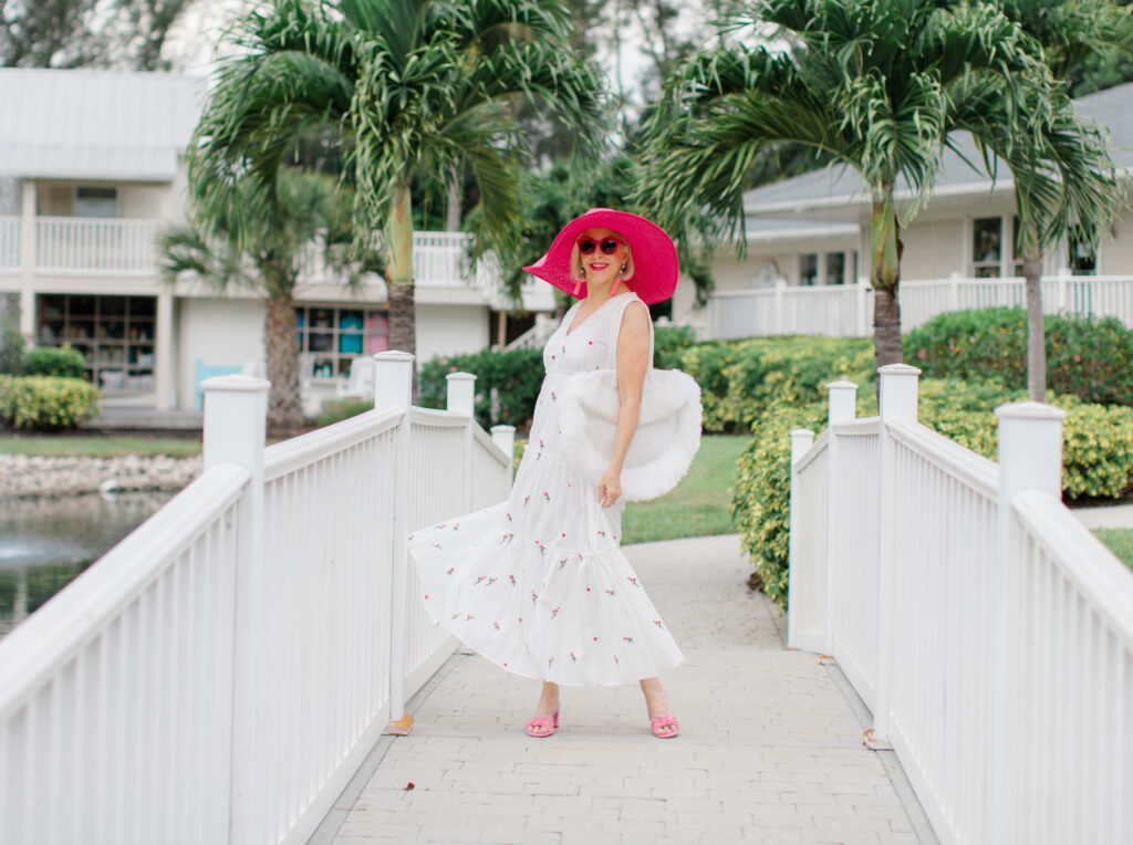 Sheree Frede of the SheShe Show walking on white bridge wearing a white maxi dress and hot pink hat