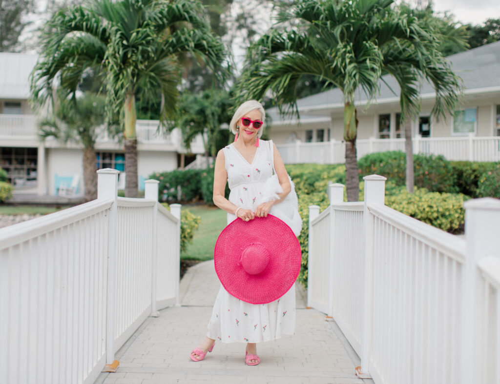 Sheree Frede of the SheShe Show walking on white bridge wearing a white maxi dress and hot pink hat