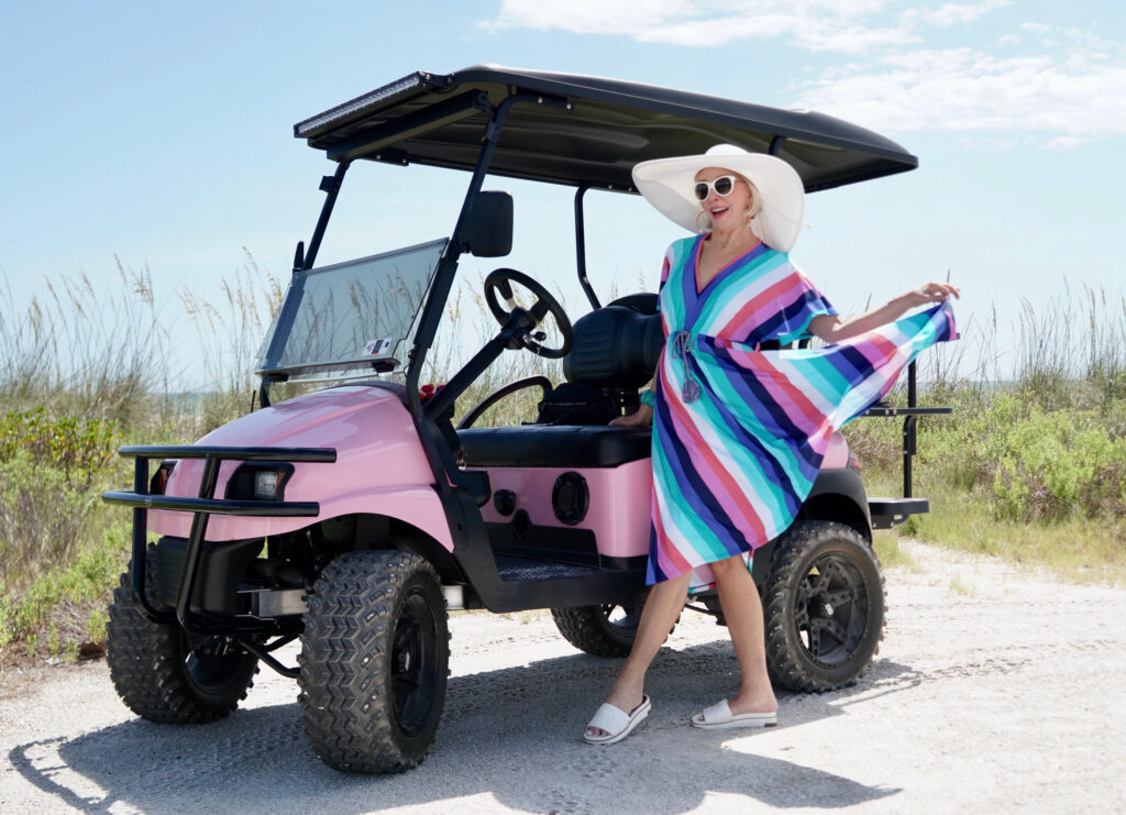 Sheree Frede of the SheShe Show wearing a multi color stripe midi dress with big white hat in pink golf cart