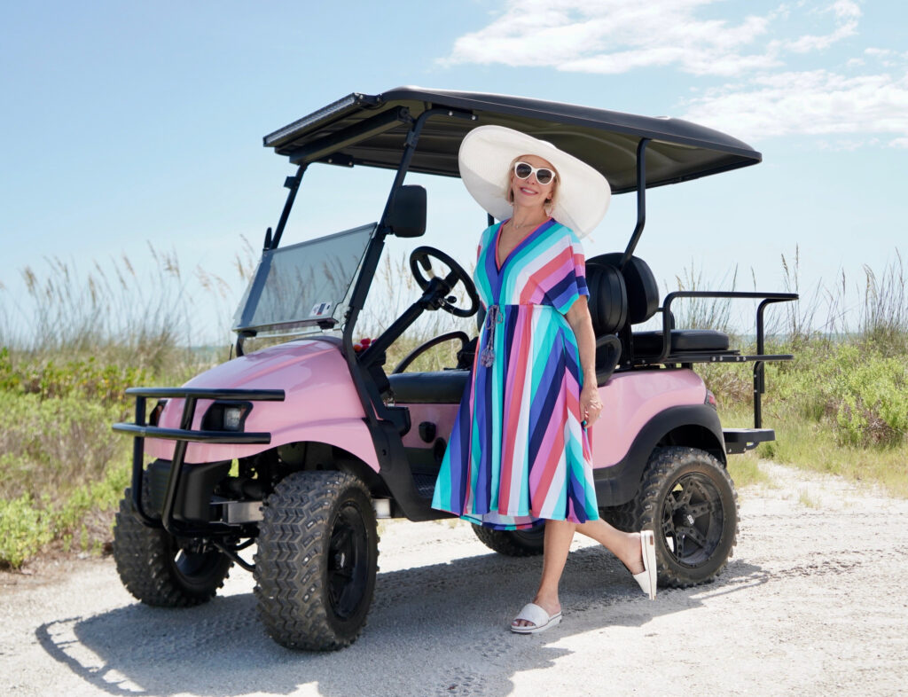 Sheree Frede of the SheShe Show wearing a multi color stripe midi dress with big white hat in pink golf cart