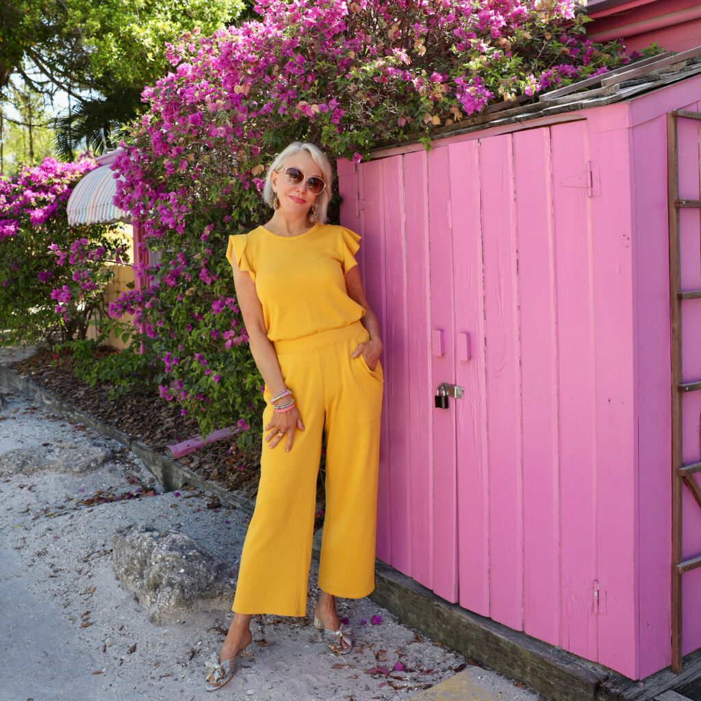Sheree Frede of the SheShe Show standing in front of pink wall wearing a yellow pants outfit