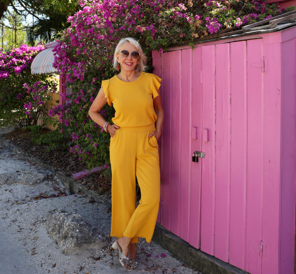 Sheree Frede of the SheShe Show standing in front of pink wall wearing a yellow pants outfit