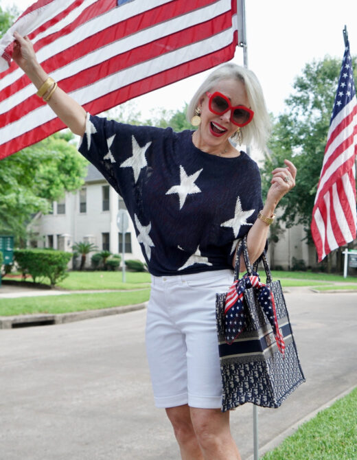 Sheree Frede of the SheShe Show standing by American flags wearing a navy and white star sweater