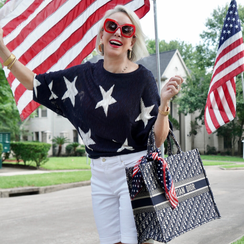 Sheree Frede of the SheShe Show standing by American flags wearing a navy and white star sweater