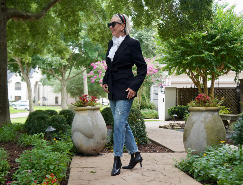 Sheree Frede of the SheShe Show standing on sidewalk wearing bule jeans, black blazer, and white bow blouse