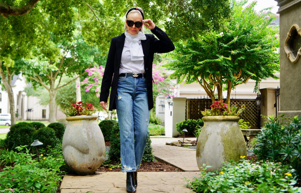 Sheree Frede of the SheShe Show standing on sidewalk wearing bule jeans, black blazer, and white bow blouse