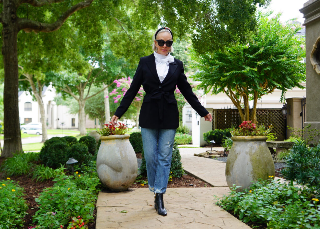Sheree Frede of the SheShe Show standing on sidewalk wearing bule jeans, black blazer, and white bow blouse