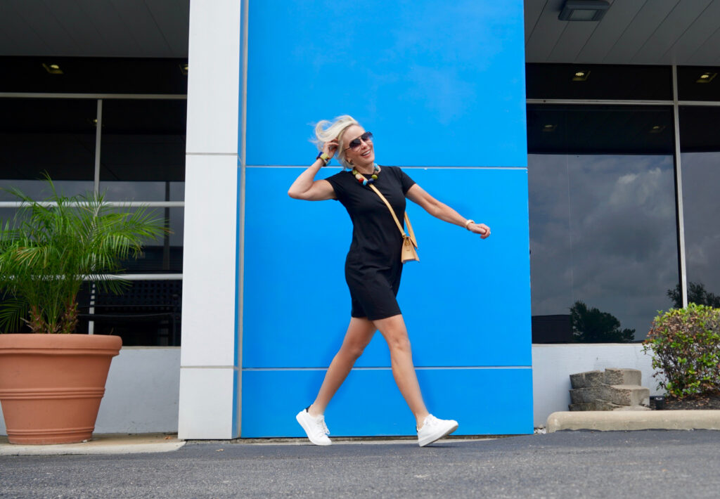 Sheree Frede of the SheSheShow standing in front of blue wall wearing a black short sleeve t-shirt dress