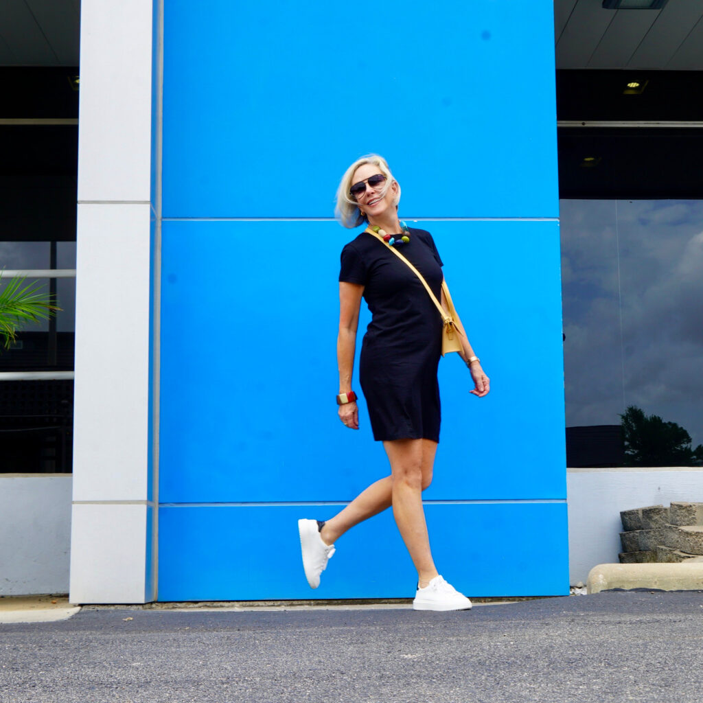 Sheree Frede of the SheSheShow standing in front of blue wall wearing a black short sleeve t-shirt dress