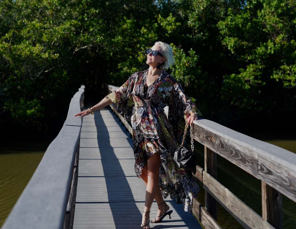 Sheree Frede of the SheShe Show standing on wood walking bridge wearing a ruffle print midi dress