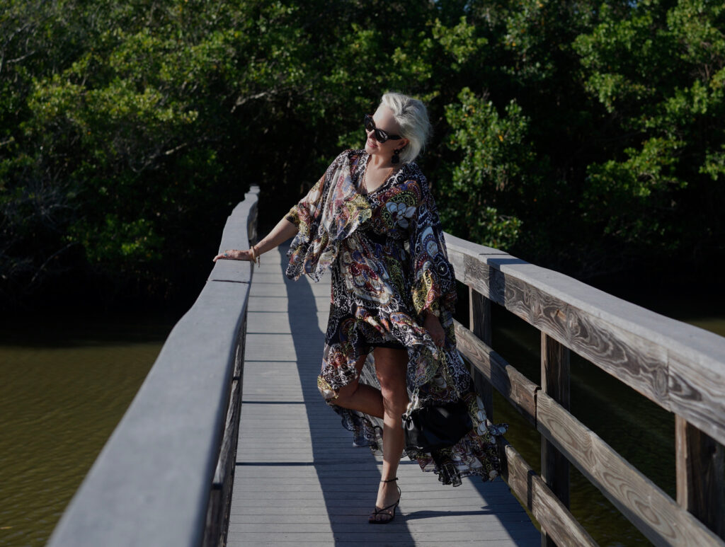 Sheree Frede of the SheShe Show standing on wood walking bridge wearing a ruffle print midi dress