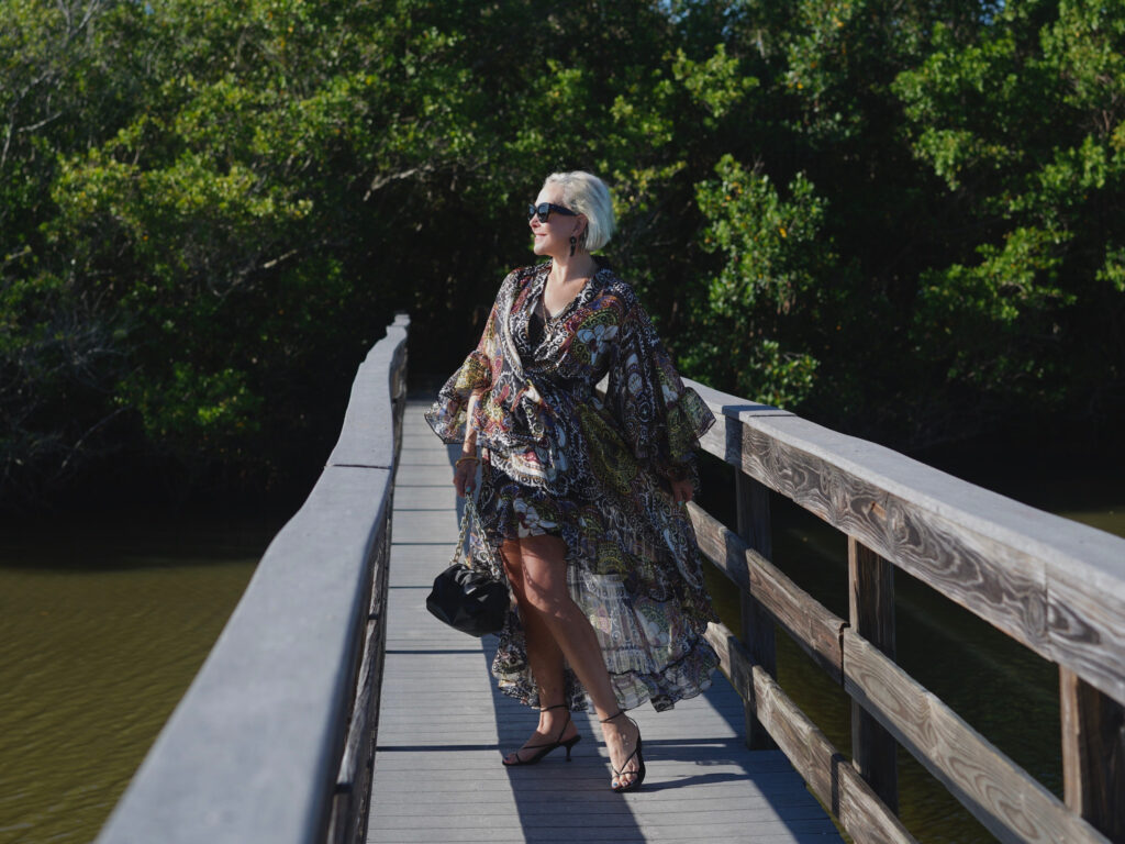 Sheree Frede of the SheShe Show standing on wood walking bridge wearing a ruffle print midi dress