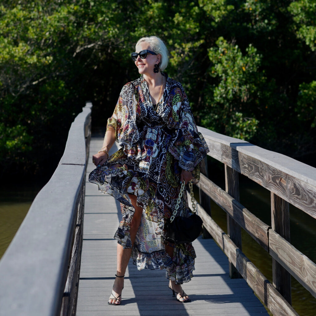 Sheree Frede of the SheShe Show standing on wood walking bridge wearing a ruffle print midi dress