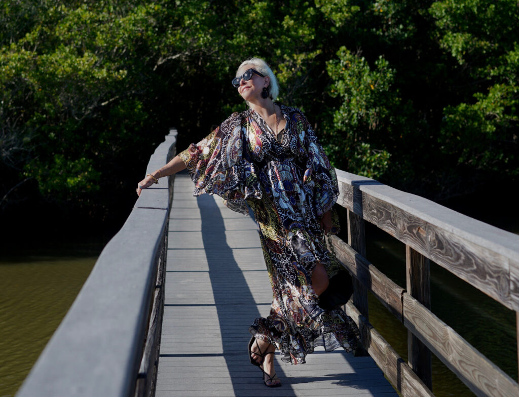 Sheree Frede of the SheShe Show standing on wood walking bridge wearing a ruffle print midi dress