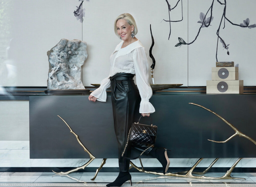 Sheree Frede of the SheShe Show walking in front of black credenza wearing black faux leather joggers and a white feminine top