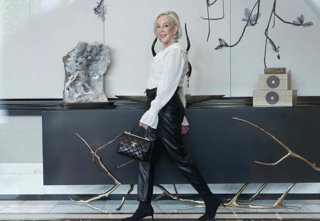 Sheree Frede of the SheShe Show walking in front of black credenza wearing black faux leather joggers and a white feminine top