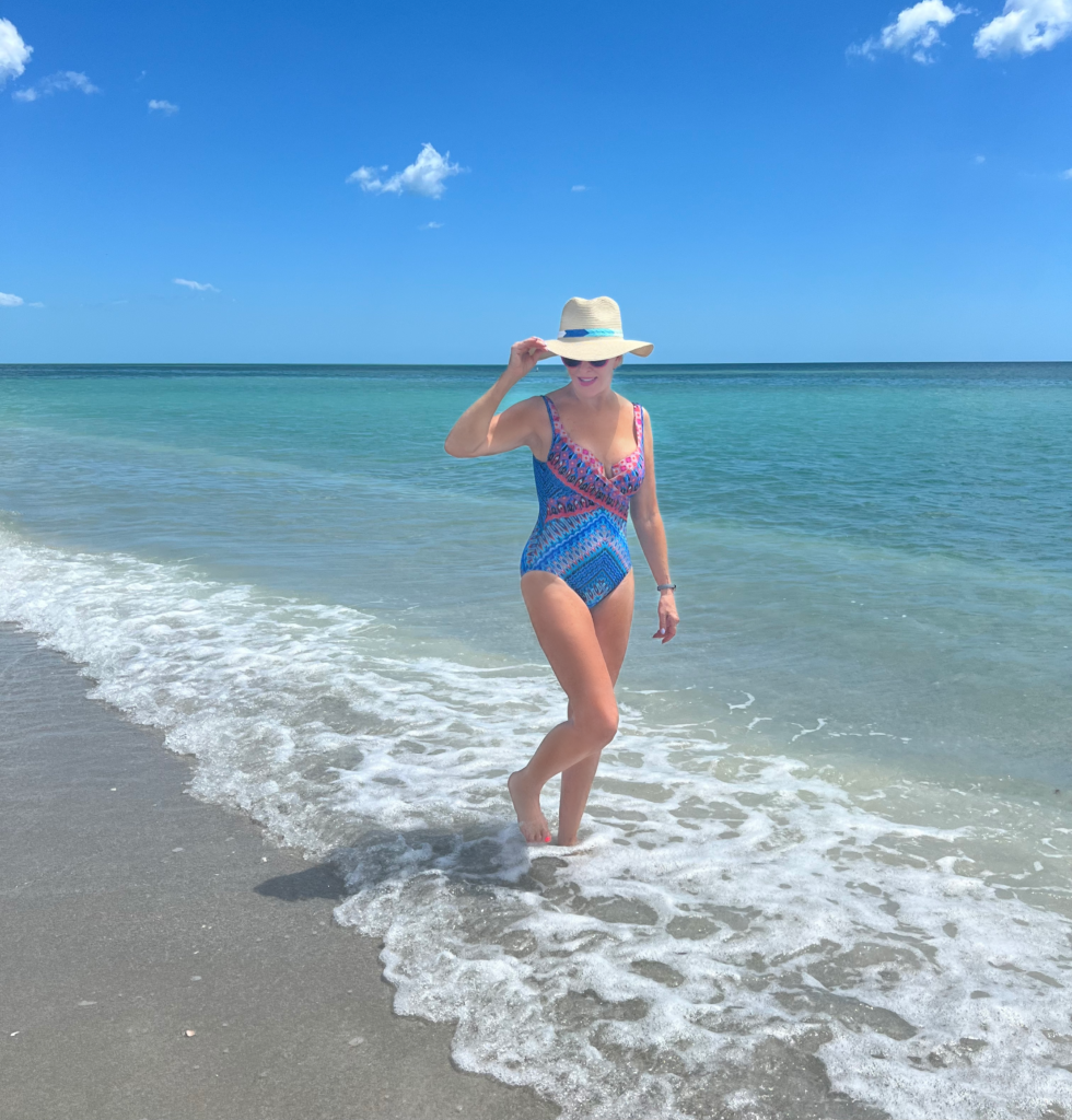 Sheree of the SheShe Show walking along the beach wearing a blue print swimsuit by Miraclesuit