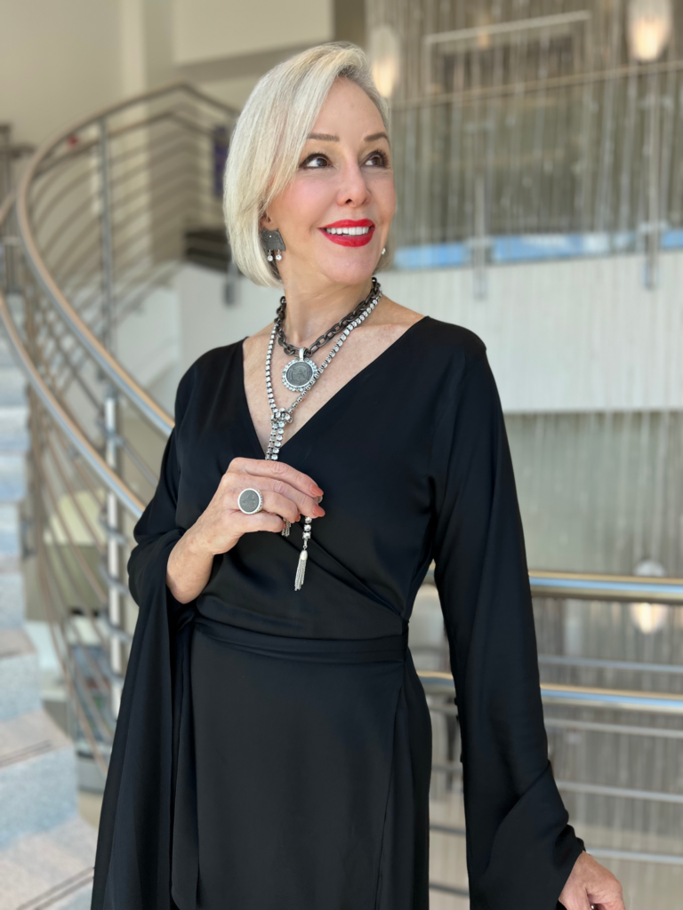 Sheree of the SheShe Show wearing a long black wrap dress with flowy sleeves with French Kande medallion jewelry