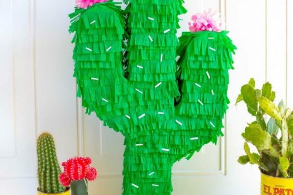 This is a photo of a cactus pinata, colorful pom pom garland and 3 mini cacti potted in metal canisters.