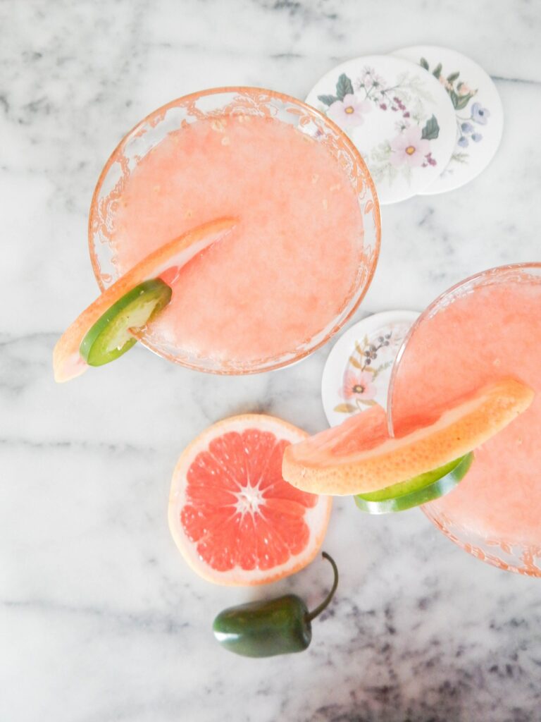 This is a photo of two frozen spicy paloma cocktails garnished with fresh grapefruits and jalapeños.