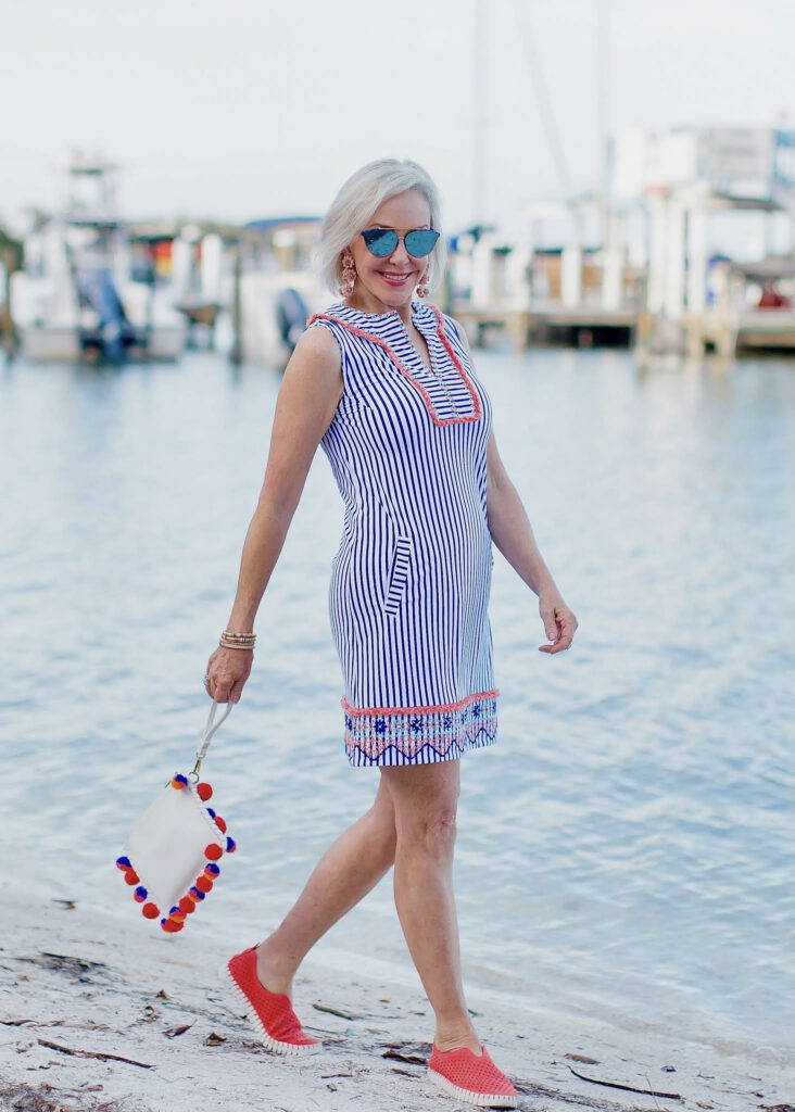 Sheree Frede of the SheShe Show standing on an ocean dock wearing a patriotic style casual Cabana Life dress that is blue and white stiped with red and blue detailing - perfect for a patriotic holiday.