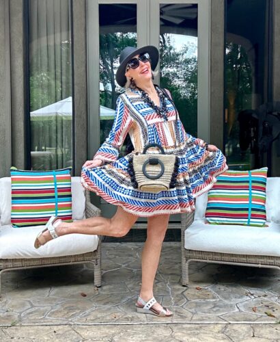Sheree Frede of the SheSheShow wearing a Festive 4th of July style outfit in a red white and blue skater dress, black hat, rattan handbag and white sandals