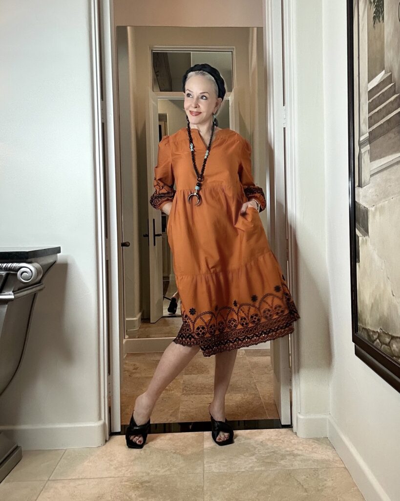 Sheree wearing a butnt orange midi dress with black embroidery trim