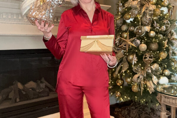 Sheree of the SheShe Show holding gifts by the Christmas tree wearing red satin pajama pant set from Soma Intimates gift ideas