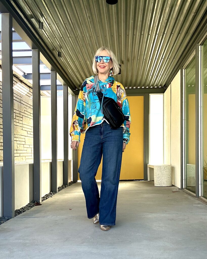 Sheree Frede of SheSheShow in bright patterned sweatshirt, jeans, and turquoise sunglasses for resort wear travel